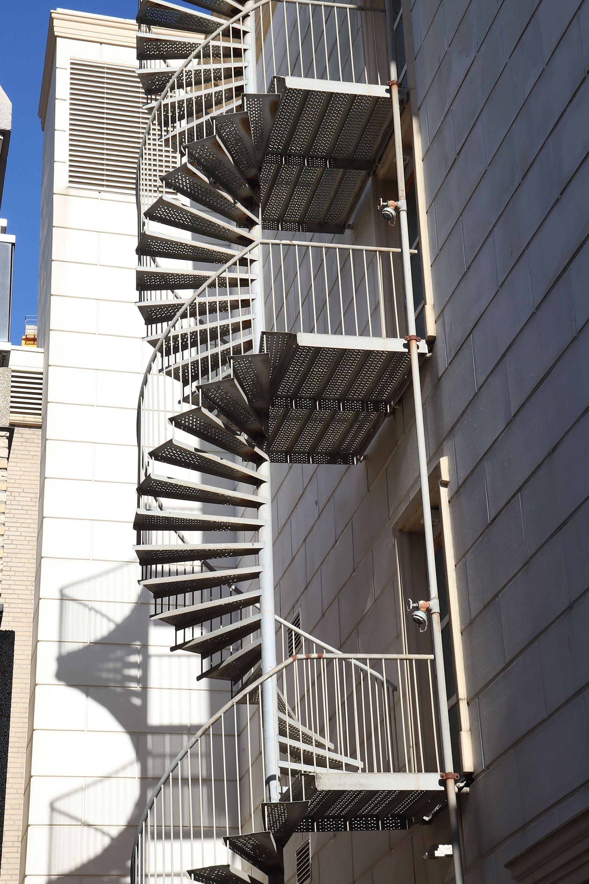 A tall spiral metal staircase on the exterior of an urban building, shot during daytime.